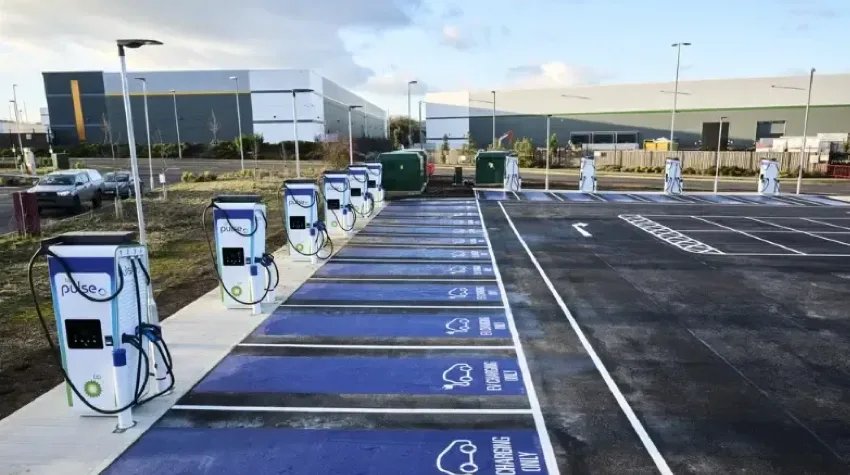 Rows of empty bp pulse chargers are lined up at the boundary of a parking lot.
