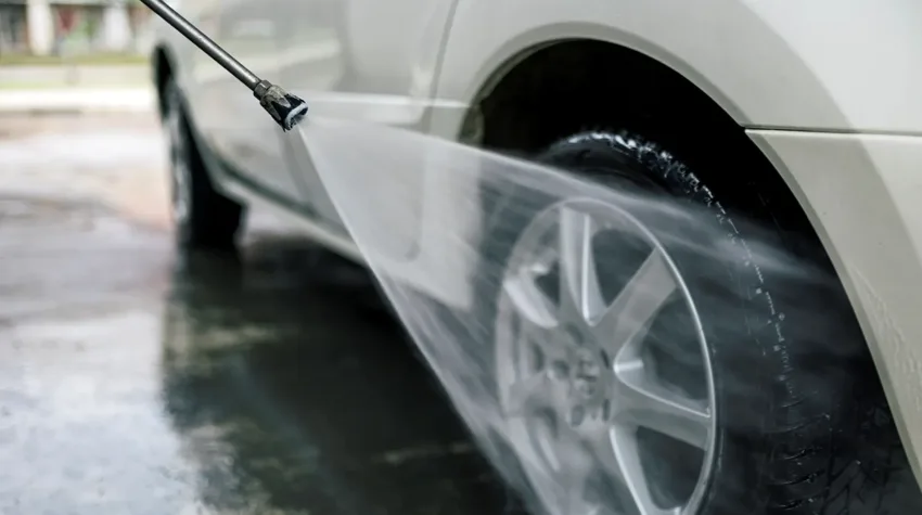 A silver car having its tyres being washed with a jet washer. 
