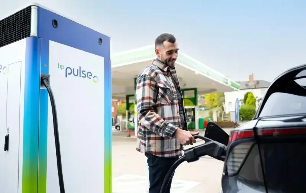A man at a bp pulse charging station, holding a charger and charging his black electric car.