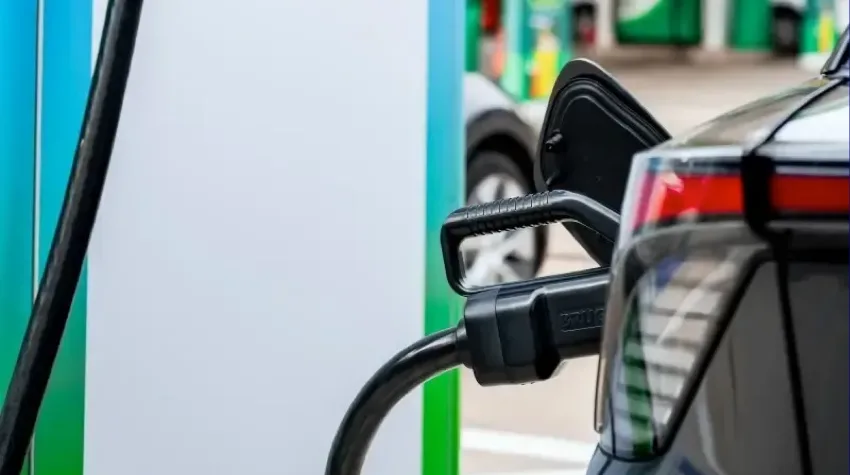 An electric charging cable plugged into a black car. Only the back left lights are visible of the car.