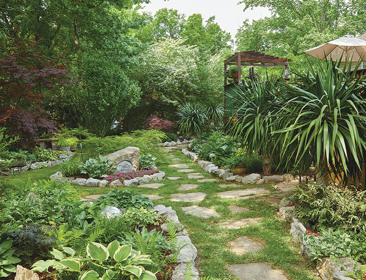 Southern shade garden backyard stone pathway: Yuccas don’t need much maintenance. Just tug off the occasional dead leaf from below the clump of foliage.