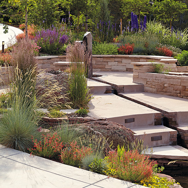 low maintenance plants CO garden:The fountain sculpture is the focal point in the center of this garden. Clumps of nearby upright perennials and ornamental grasses form similar shapes that tie it all together.