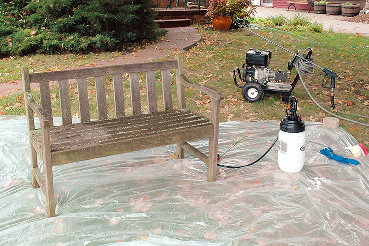 Wooden garden bench in yard on plastic tarp with power sprayer: Prep your area by putting down a plastic tarp on the lawn as wood brightening solutions can bleach your driveway.