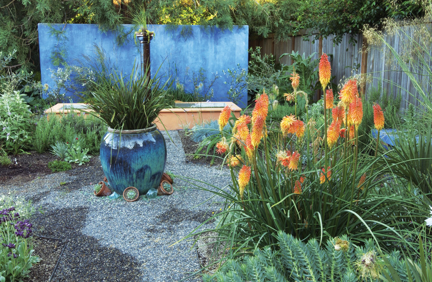 Torch lily paired with blue garden accents: Create a complementary color contrast when you set luminous torch lily flowers against a blue background. Add color echos with hardscaping elements, such as the terra-cotta orange-hued pond wall and blue container. 
