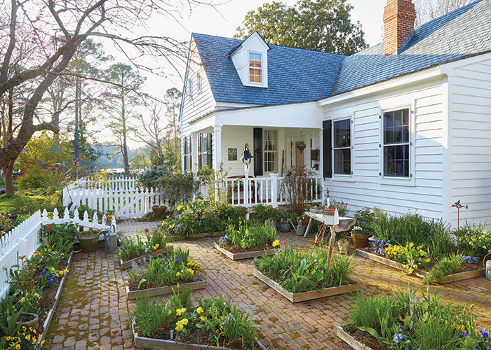 Front garden beds with tulips and white picket fence: A low picket fence creates a friendly welcome and helps define the entry patio. Raised beds full of herbs, vegetables and flowers make it easy to grab what you need and get back to cooking.