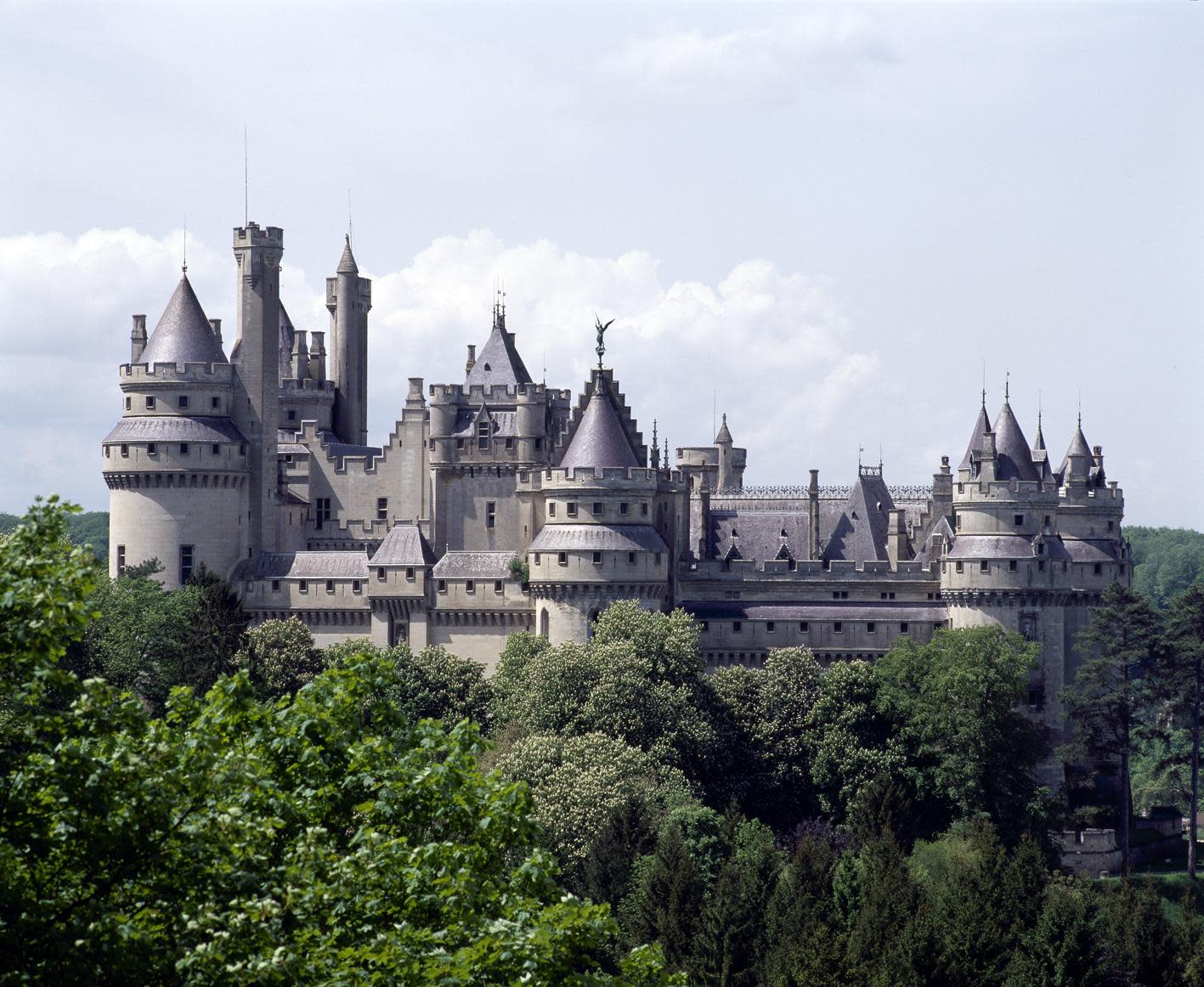 A distant view of the The fairytale Chateau de Pierrefonds surrounded by a forest