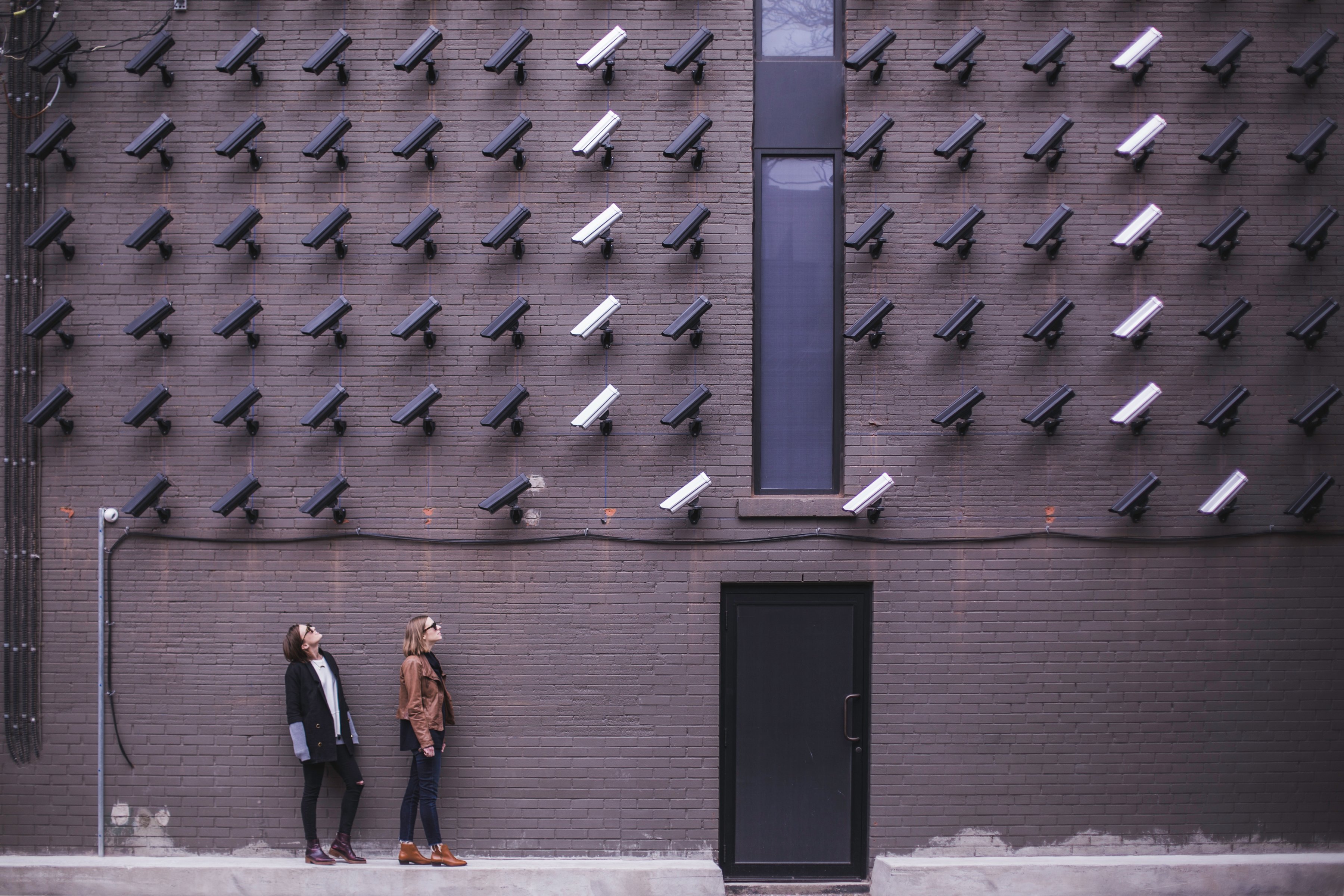 Two women facing wall of multiple security cameras
