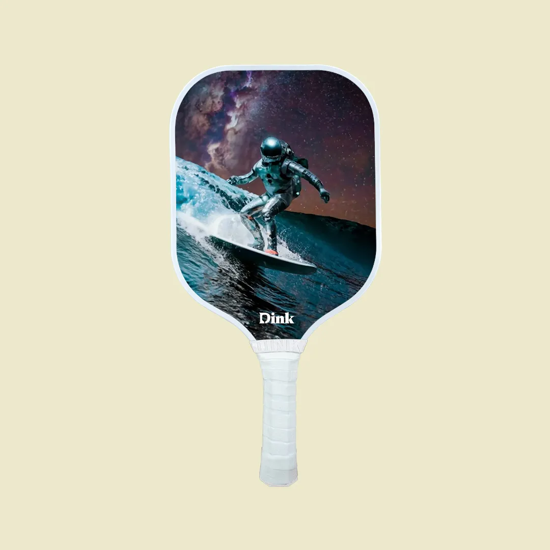 A custom pickleball paddle from Dink with an astronaut surfing under the starry sky