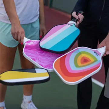 four pickleball players holding four different personalized pickleball paddles from Dink with colorful designs