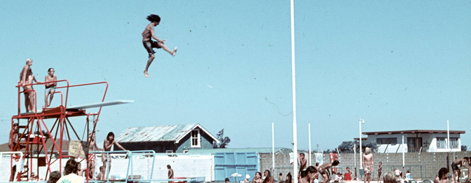 A boy jumping from a diving board into a swimming pool.