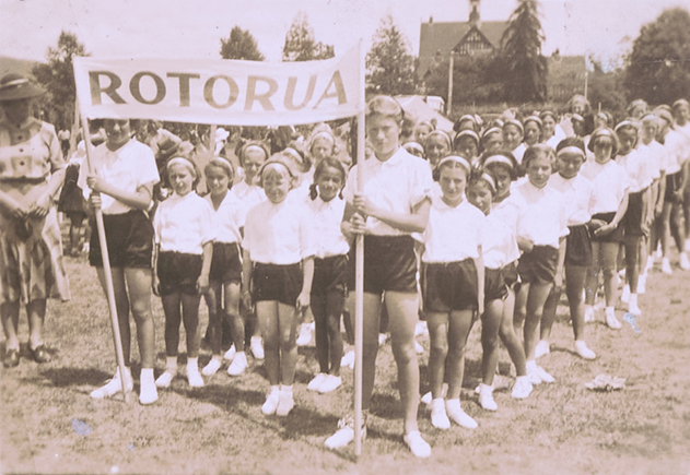 A group of children wearing sports uniforms lined up behind a banner with the word 'Rotorua'.