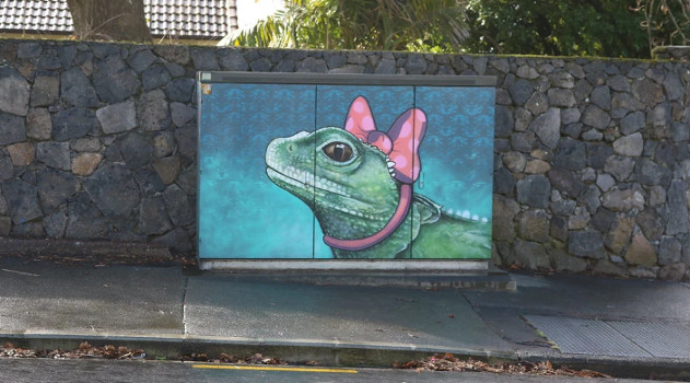 An outdoor mural of a tuatara wearing a pink bow.