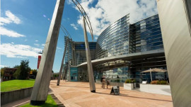 Modern multi-storey building with a curved glass facade, metal supports, and a walkway leading to the entrance.