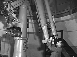 A large observatory telescope, with a person adjusting the eyepiece while standing beneath the instrument.