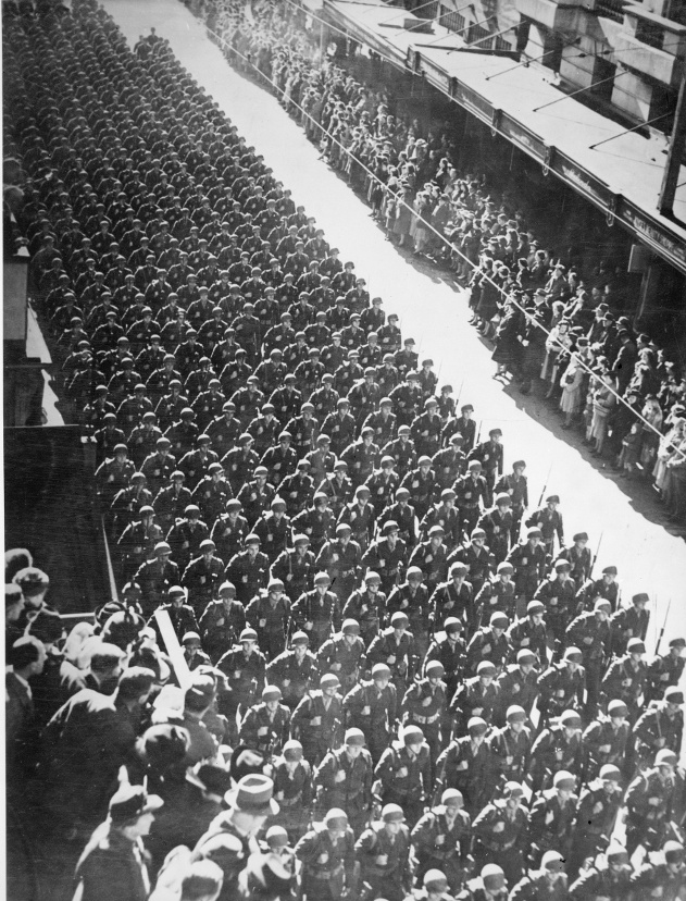 Troops marching down a street lined with people.