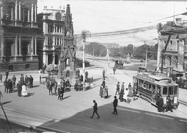 A city square with a tram and pedestrians.