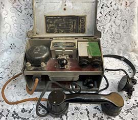 Rectangular green metal box container with hinged lid containing field telephone - handset, headset and controls.