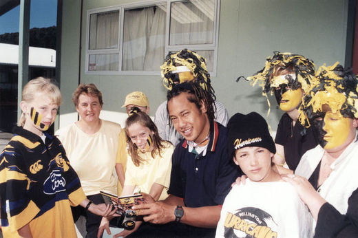 Rugby player Tana Umaga surrounded by children wearing Hurricanes t-shirts and yellow and black face paint.