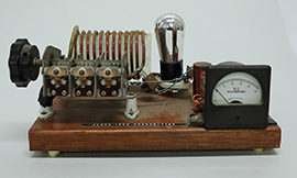 Vintage radio transmitter with coils, a vacuum tube, and an analog meter on a wooden base.