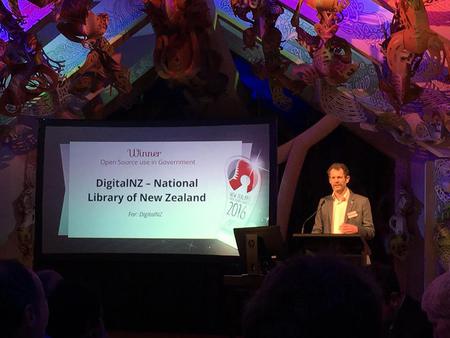 A man standing at a podium with a screen showing 'Winner: DigitalNZ - National Library of New Zealand'.