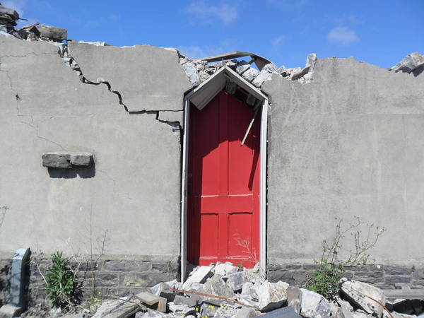 A red door in a crumbling concrete building.
