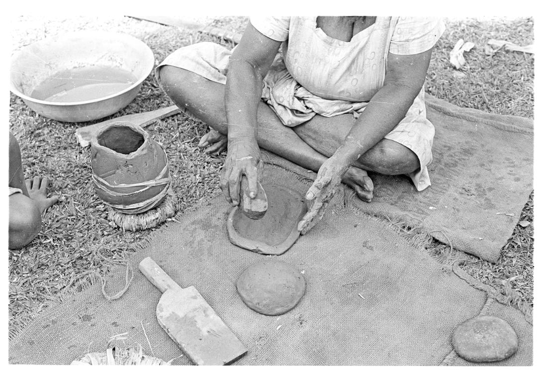 Cropped photo of a woman sitting cross legged on the ground making a plate from clay.