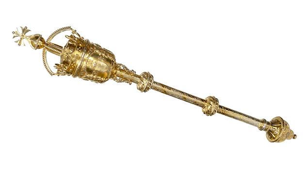 An ornate gold ceremonial mace with intricate detailing along the shaft and a decorative crown-like head.