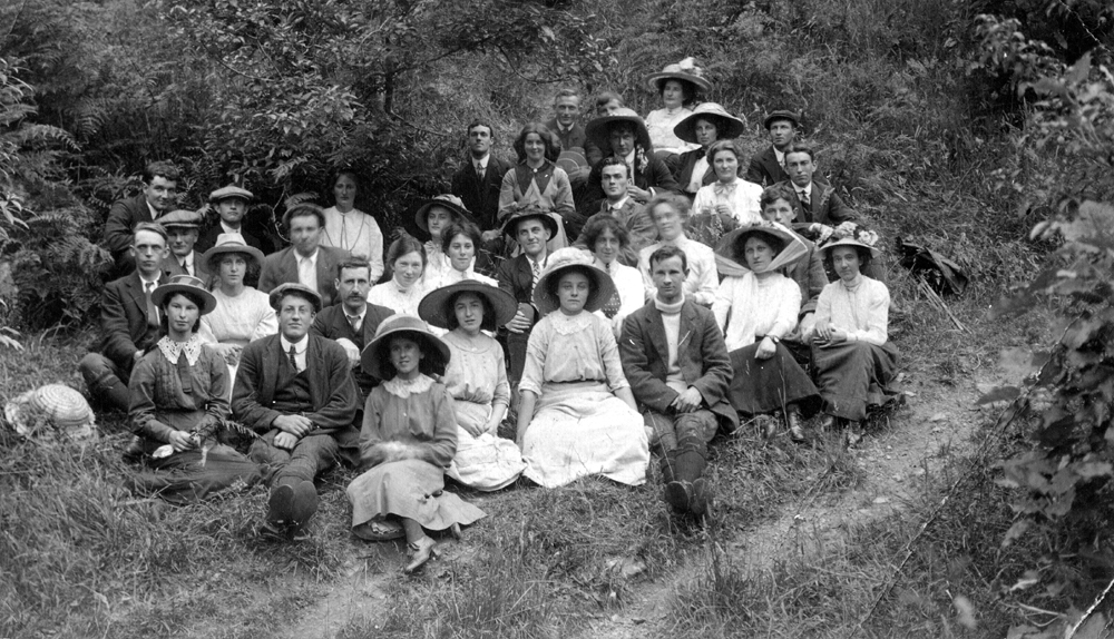 A group of people wearing Edwardian style clothing sitting on a grassy bank.