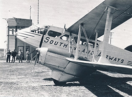 South Island Airways aircraft on the ground near a small control tower, with several people standing in the background.