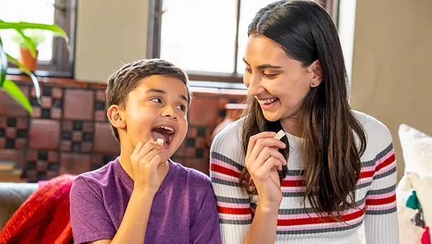 Mother and son smiling at each other while son eats a trident gum piece.