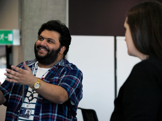 A young man gestures to a board while having a discussion with a woman about its contents