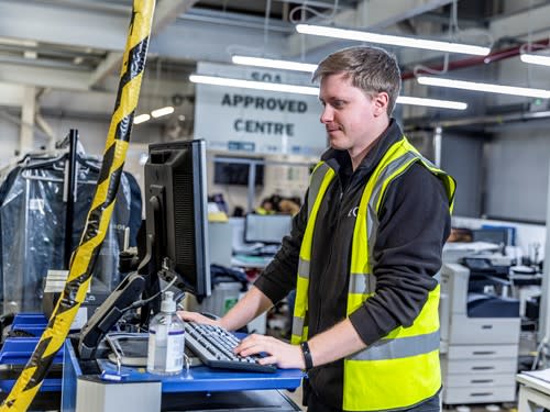 A young man in a hi-vis vest stands at a computer