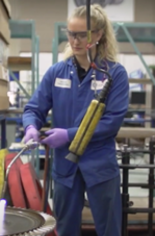 Young woman in blue overalls holds a welding torch while working in a factory