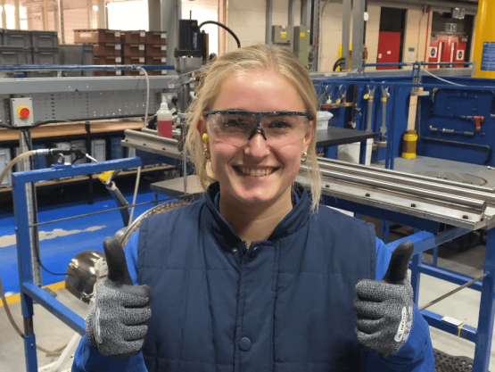 Young woman wearing safety goggles smiles and gives a thumbs up to the camera
