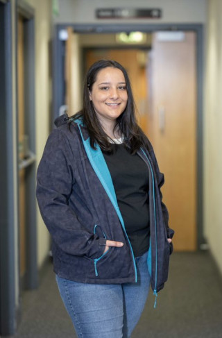 Young woman in a blue jacket  stands in a corridor and smiles to the camera