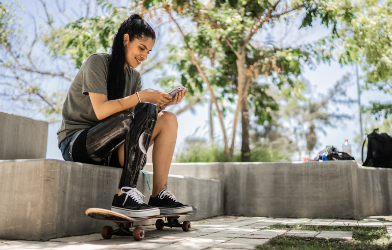 Woman sitting at skate park smiling at phone
