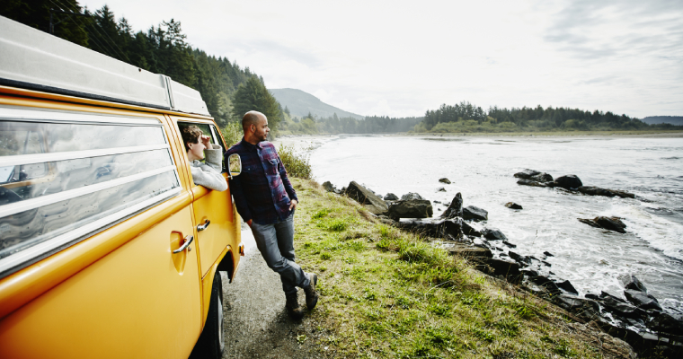 A man leaning on a VW van, pulled over on the side of a road