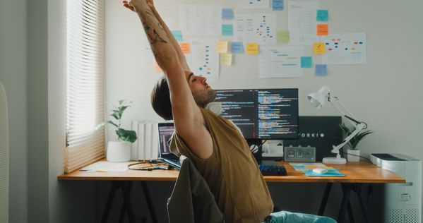 A man sitting in his home office chair, having a stretch