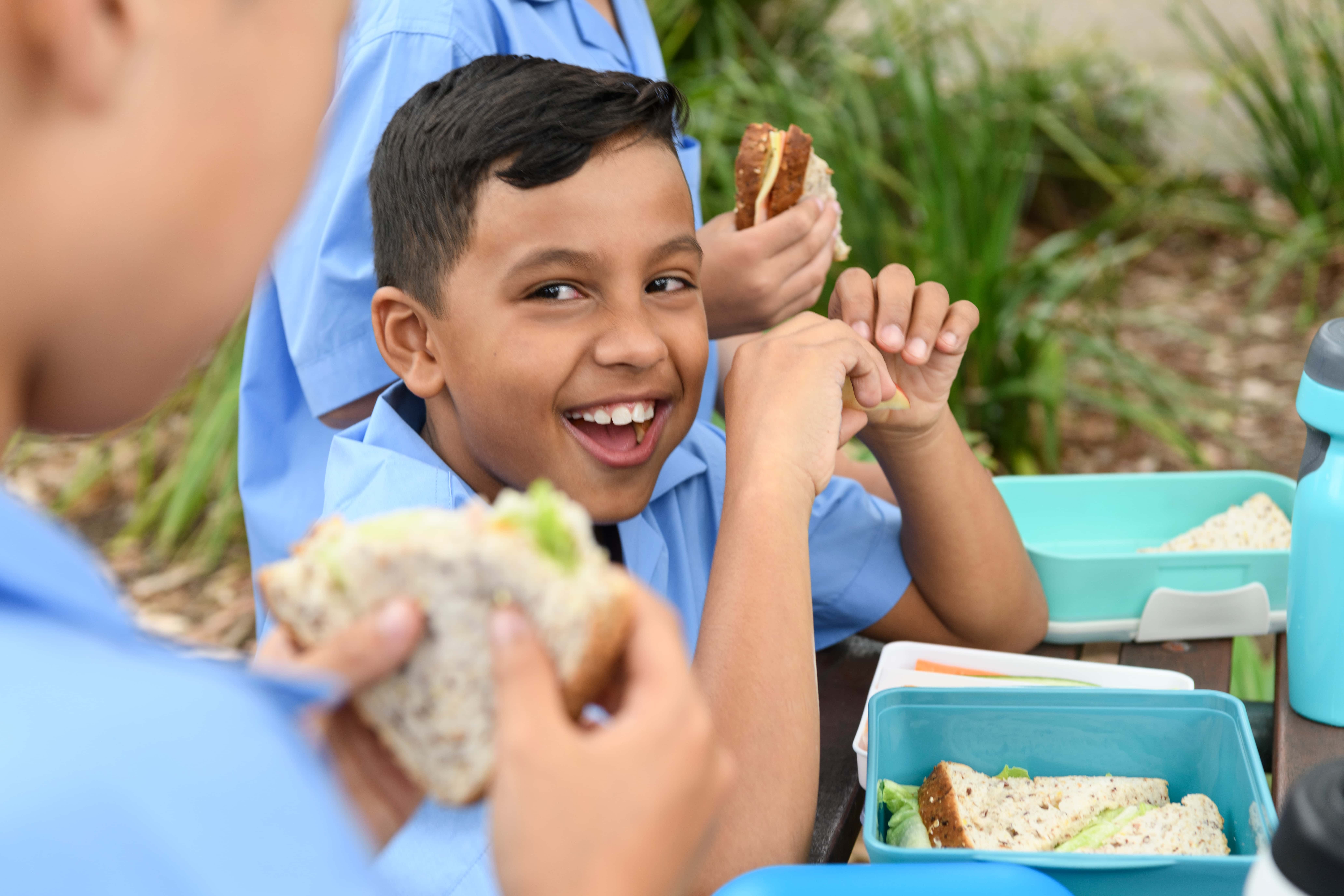 Kid at school eating a sandwich surrounded by friends.