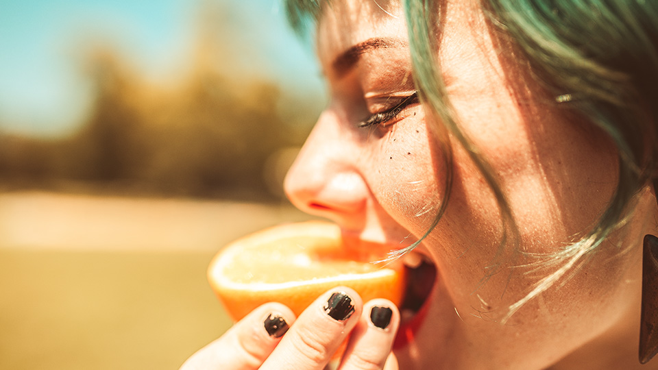 A young woman smiles as she bites into half an orange