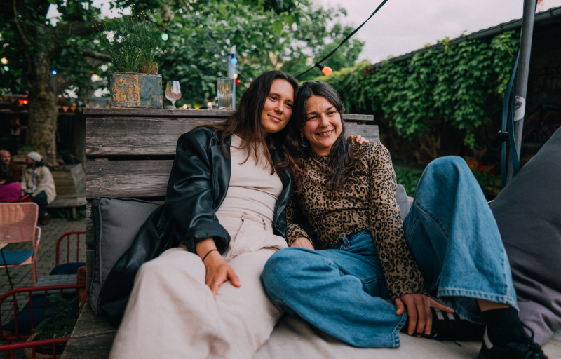 Two women sitting close to each other on an outside chair.