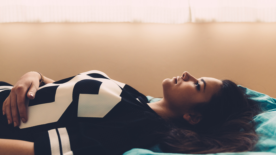 Young international student laying on her bed wearing a white and black knit