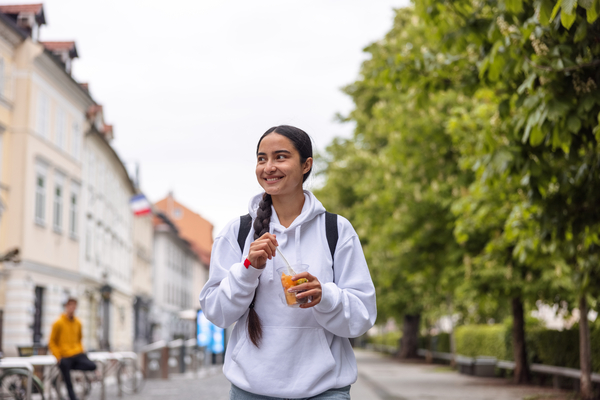 A young girl walks down the street with orange juice smiling