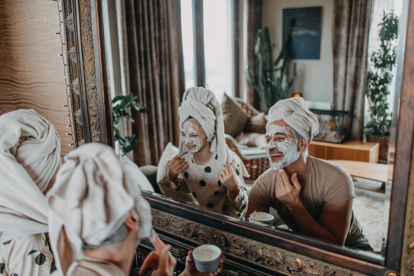 Woman and man wearing beauty face masks smiling in mirror