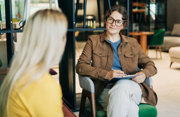 A professional female psychological consultant listens to a client while sitting at her workplace
