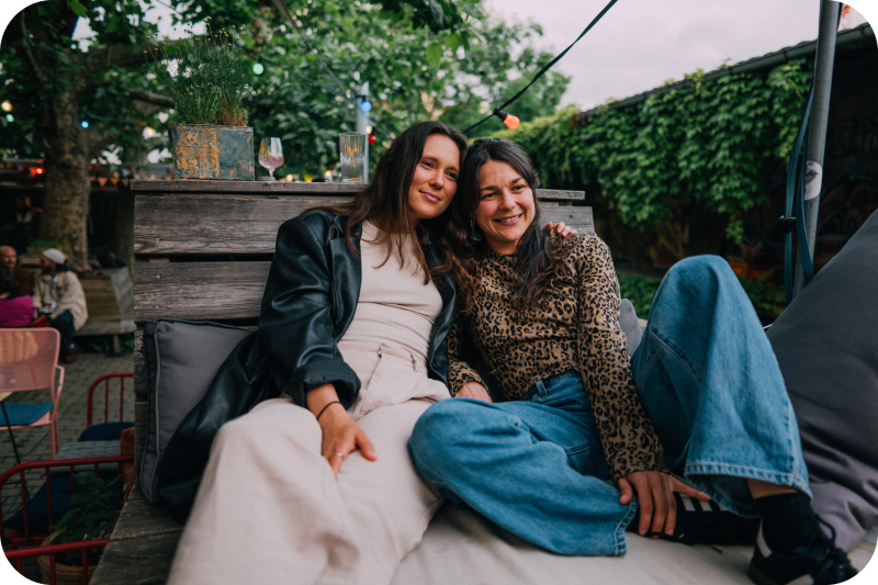 Two women sitting close to each other on an outside chair.