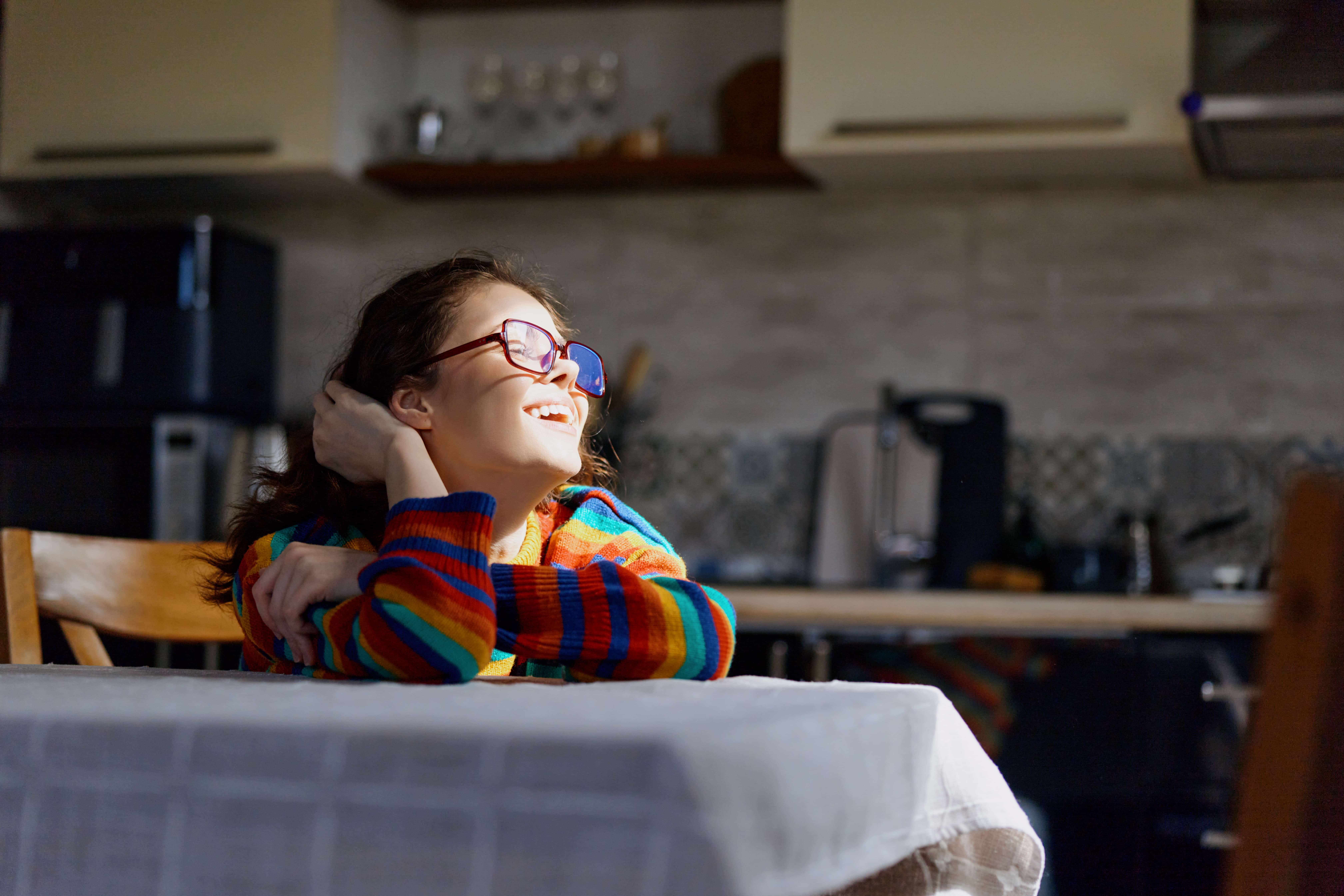 Person leaning on a kitchen table, smiling towards the sun.