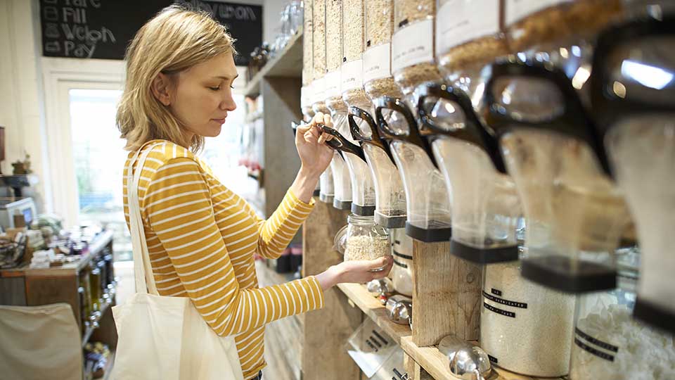 A woman pouring oats into a jar at a health food store.