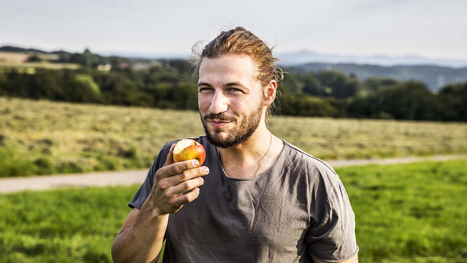 Young man eating an apple in a park.