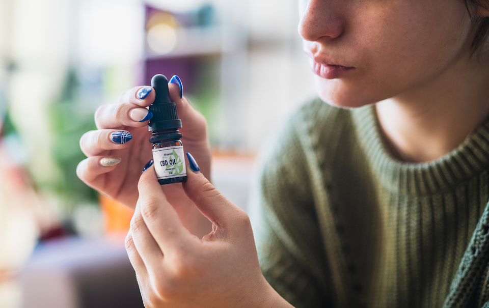 Close-up of a person holding a CBD oil bottle with dropper. Their face is not in frame,